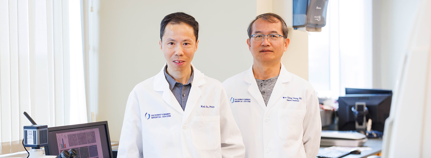 Two researchers wearing white coats and standing in a laboratory.